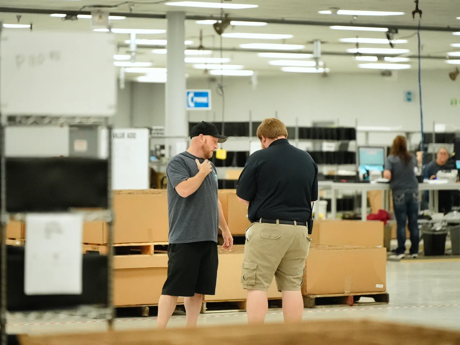 Refreshed Tech team members on the warehouse floor beside pallets of devices, with grading and testing stations behind them